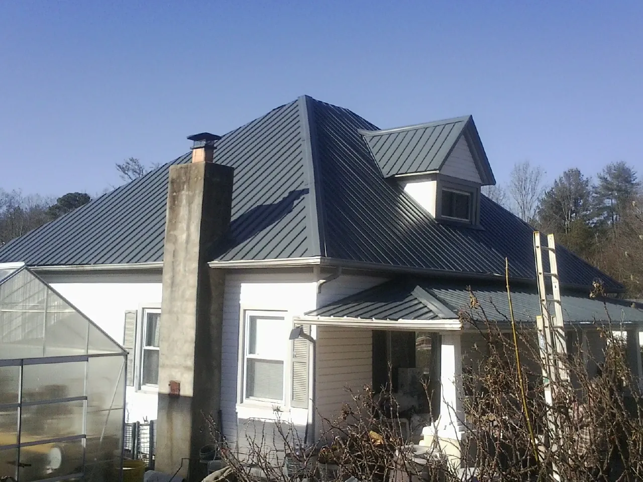 Dark blue standing seam metal roof on a white farmhouse with dormer — Slate & Tile Roof Repair by Roofing Brothers in Bellerose