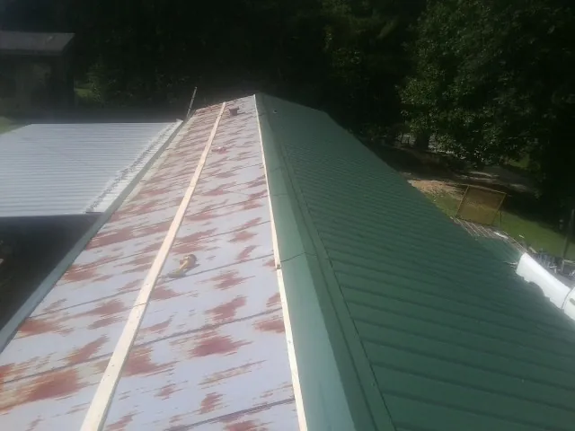Old rusted panels beside newly installed green metal roofing — Wind Damage Roof Repair by Roofing Brothers in Bellerose