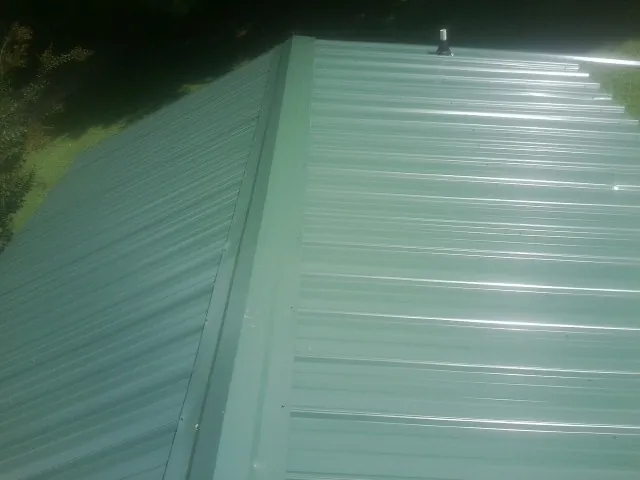 New green metal panels meeting at the ridge of a roof — Flat Roof Repair work by our crew in Bellerose