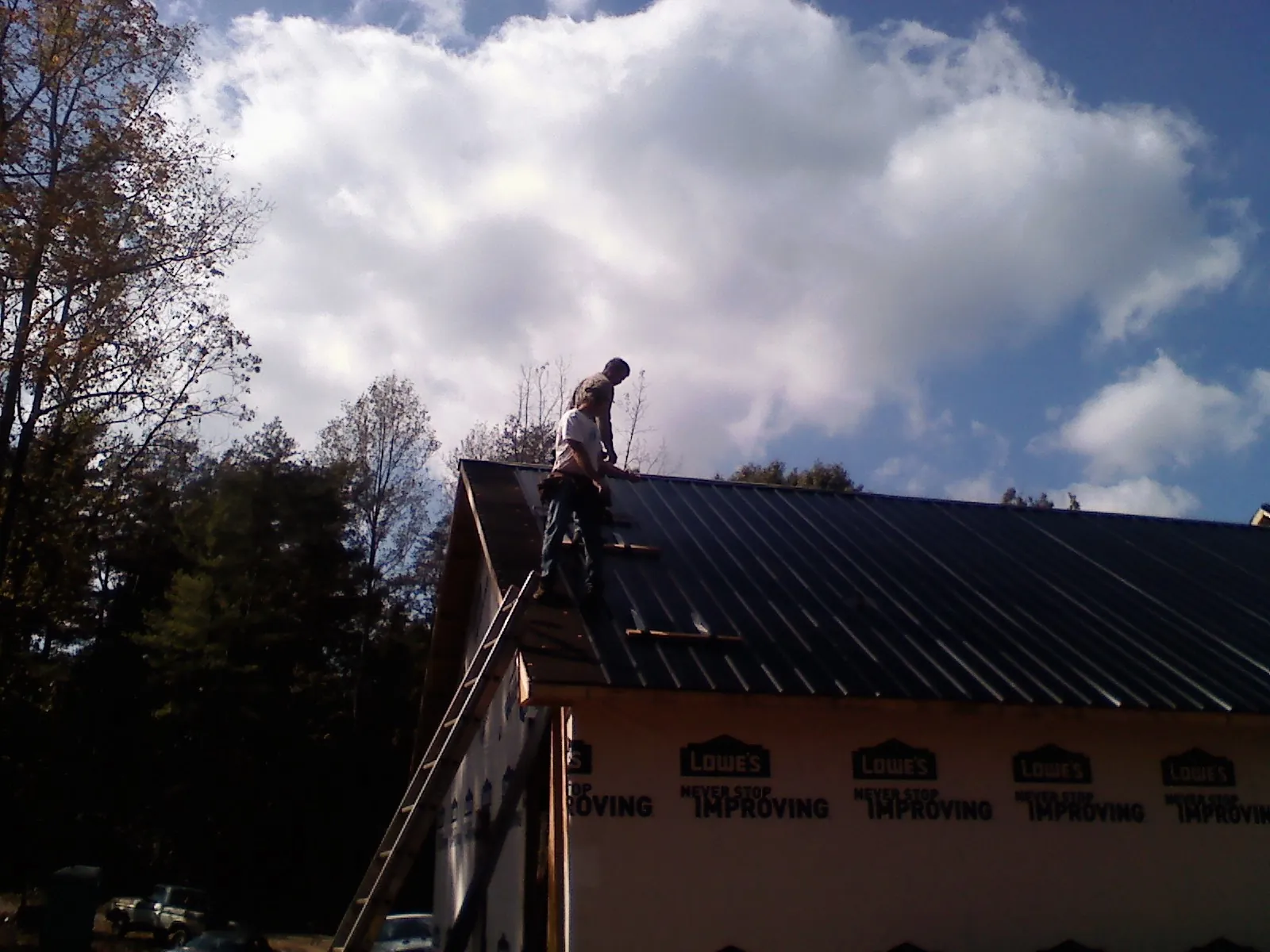 Roofer fastening dark metal panels high against a cloudy sky, from a Roof Inspection job in Bellerose