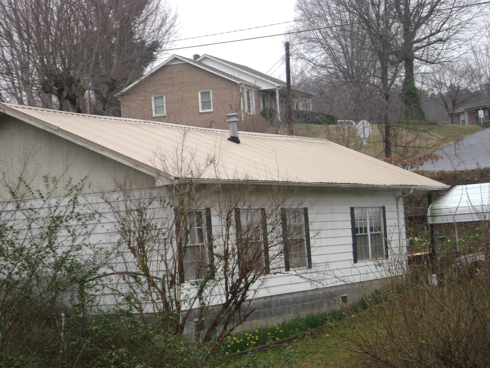 Tan metal roof on a white sided house set into a hillside — Commercial Roofing by Roofing Brothers in Bellerose