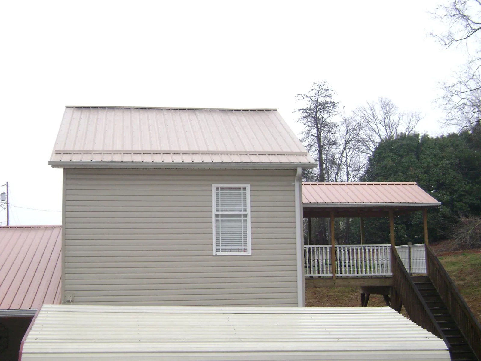 Tan metal roofs on a two story addition and attached porch, from a Roof Replacement job in Bellerose