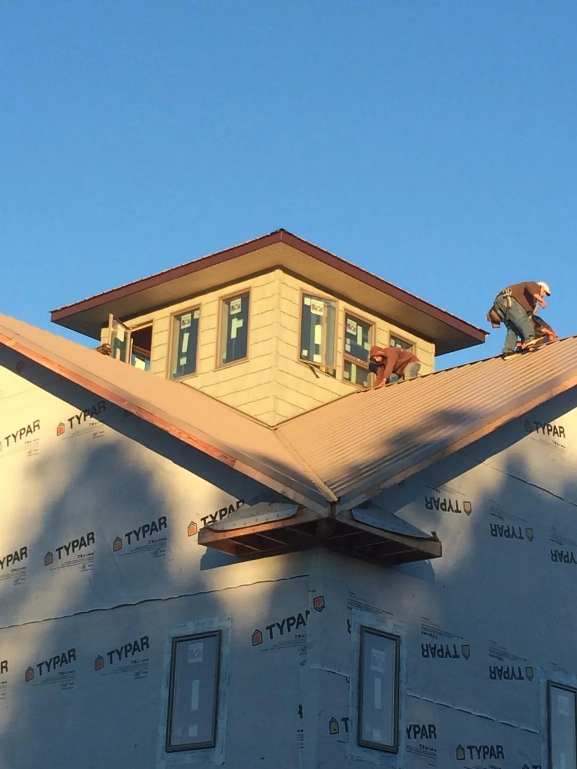 Roofers working around a rooftop cupola on a new metal roof at sunset in Bellerose